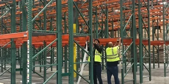 Two men in safety vests are working on a warehouse.