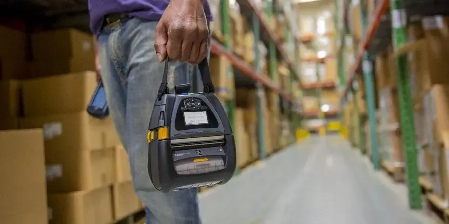 A person holding a handheld printer in a warehouse.